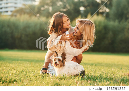 Positive emotions, on the green grass. Mother with her daughter and cute dog are on the field outdoors 128591285