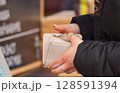 Close-Up of Hands Holding a White Wallet in a Shopping Environment 128591394