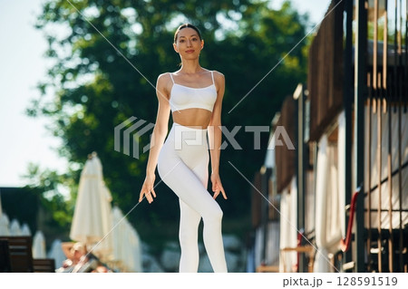 Resort exterior behind. Young woman in yoga clothes is outdoors 128591519
