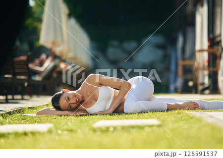 Resort exterior behind. Young woman in yoga clothes is outdoors Resort exterior behind. Young woman in yoga clothes is outdoors 128591537
