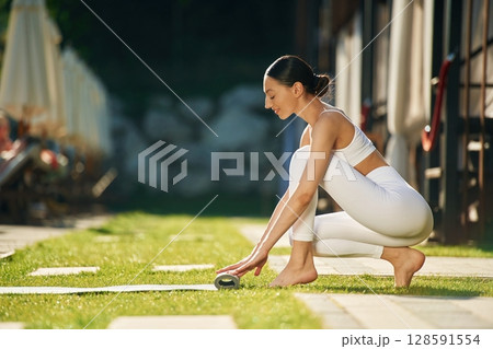 Opening the mat. Young woman in yoga clothes is outdoors 128591554
