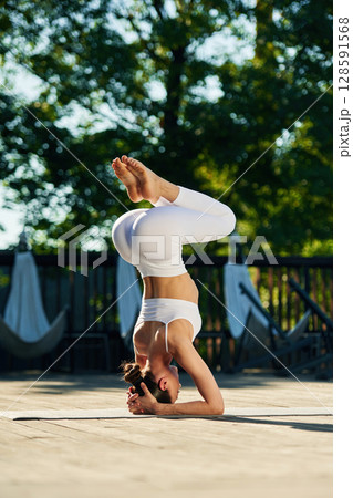 On the head, doing exercise. Young woman in yoga clothes is outdoors On the head, doing exercise. Young woman in yoga clothes is outdoors 128591568