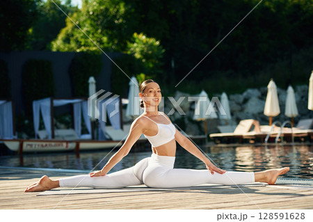 Flexible body. Woman near pool is doing yoga exercises 128591628