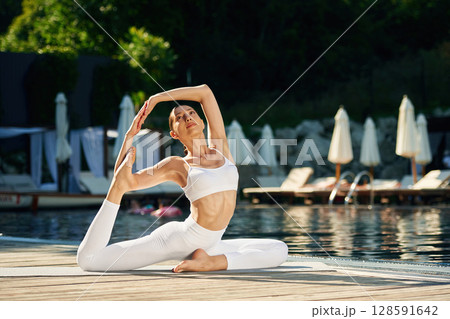 Front view. Woman near pool is doing yoga exercises Front view. Woman near pool is doing yoga exercises 128591642