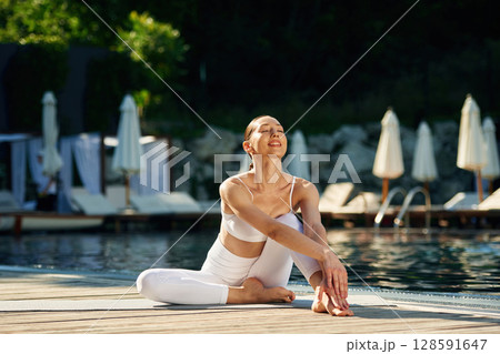 Front view. Woman near pool is doing yoga exercises Front view. Woman near pool is doing yoga exercises 128591647