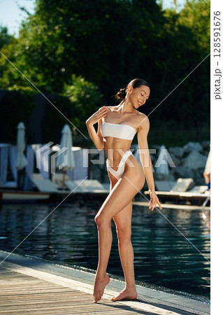 Trees with green leaves at background. Woman in white underwear is near the pool 128591676