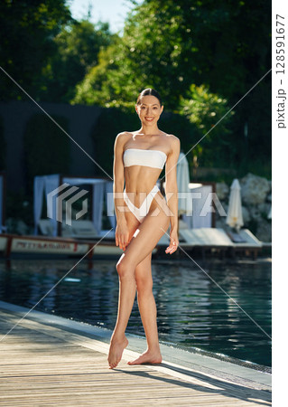 Trees with green leaves at background. Woman in white underwear is near the pool 128591677