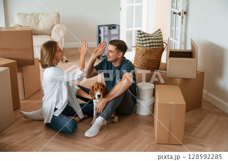 Conception of success. Sitting on the floor. Young couple with dog are moving to new home Conception of success. Sitting on the floor. Young couple with dog are moving to new home 128592285