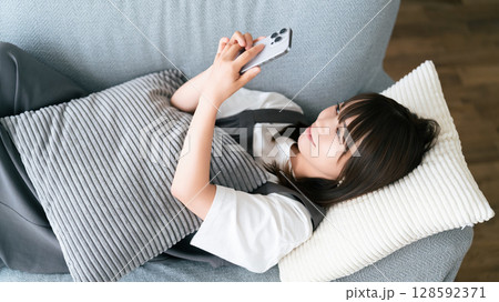 ソファに寝転んでスマートフォンを使う女性 ソファに寝転んでスマートフォンを使う女性 128592371