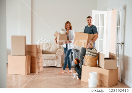 Walking forward with boxes. Young couple with dog are moving to new home 128592416