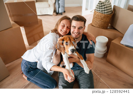 Sitting and smiling. Young couple with dog are moving to new home 128592441