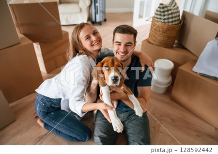 Sitting and smiling. Young couple with dog are moving to new home 128592442