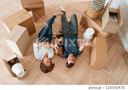 Happy young couple with dog are moving to new home. Lying down on the floor Happy young couple with dog are moving to new home. Lying down on the floor 128592470