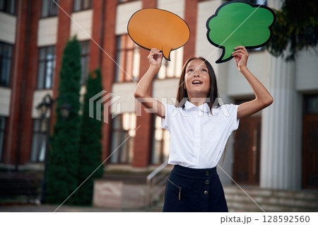 Colorful stickers in hands, copy space for text, thoughts. School girl in uniform is outdoors near the building Colorful stickers in hands, copy space for text, thoughts. School girl in uniform is outdoors near the building 128592560