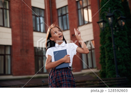 Thinking, thoughtful look. School girl in uniform is outdoors near the building Thinking, thoughtful look. School girl in uniform is outdoors near the building 128592603
