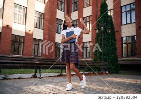 Thinking, thoughtful look. School girl in uniform is outdoors near the building 128592604