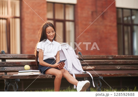 School girl in uniform is outdoors near the building School girl in uniform is outdoors near the building 128592688