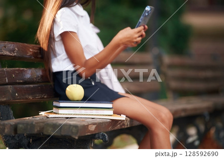 Using smartphone. School girl in uniform is outdoors near the building 128592690
