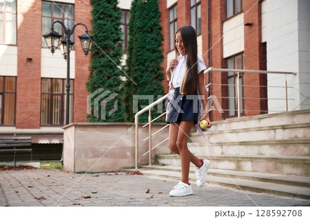 Going out from the building. School girl in uniform is outdoors 128592708