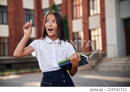 Thinking, having an idea. School girl in uniform is outdoors near the building 128592722