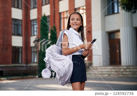 In classic uniform. School girl is outdoors near the building 128592738
