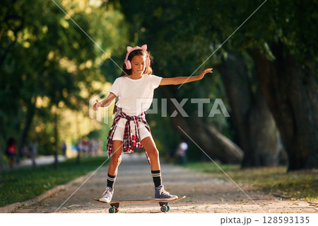Controlling the balance. Happy little girl with skateboard outdoors 128593135