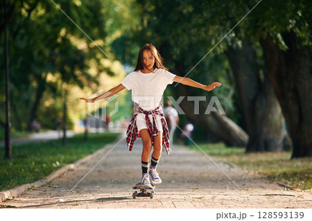 Controlling the balance. Happy little girl with skateboard outdoors 128593139