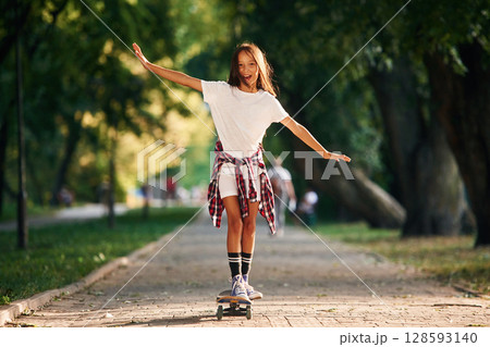 Controlling the balance. Happy little girl with skateboard outdoors 128593140