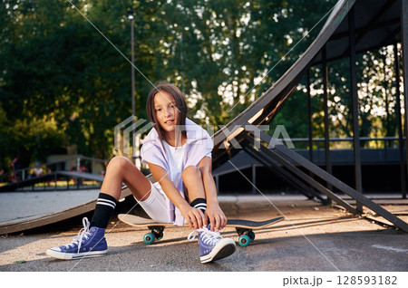 Beautiful summer time in the park, sitting. Happy little girl with skateboard outdoors 128593182
