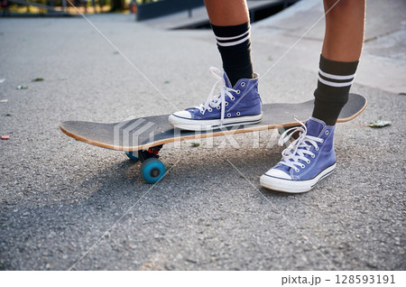 Standing on skateboard on one leg. Close up view of a young girl legs in blue shoes 128593191