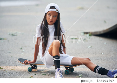 Sitting on the skateboard. Happy little girl is outdoors 128593197