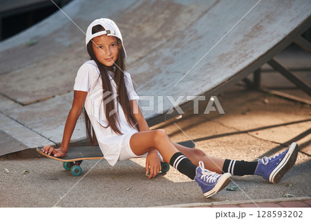 Sitting on the skateboard. Happy little girl is outdoors 128593202
