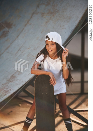 Standing with skateboard. Happy little girl is outdoors Standing with skateboard. Happy little girl is outdoors 128593210