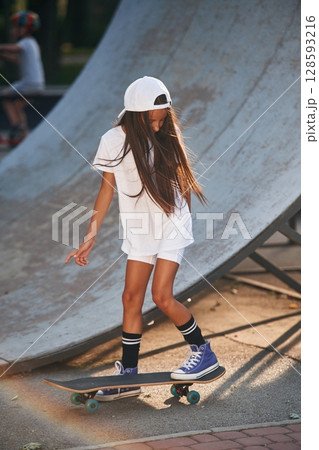 Riding skateboard near the ramp. Happy little girl with is outdoors 128593216