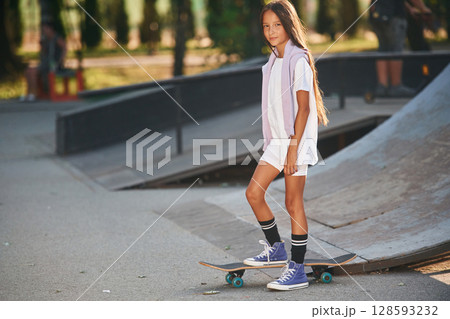 In the extreme sports park. Happy little girl with skateboard outdoors In the extreme sports park. Happy little girl with skateboard outdoors 128593232
