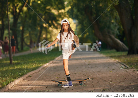On the road in park. Happy little girl with skateboard outdoors On the road in park. Happy little girl with skateboard outdoors 128593262