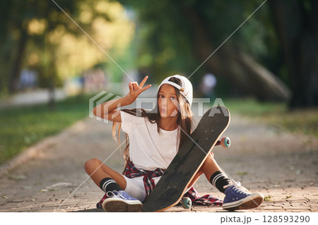 Front view, showing gestures. Happy little girl with skateboard outdoors 128593290