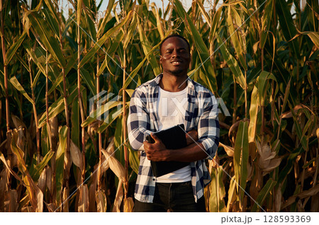 Farmer is with notepad. Young black man is standing in the cornfield at daytime 128593369