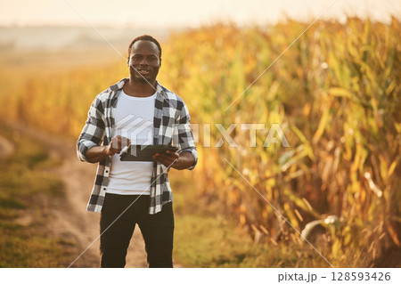 Holding digital tablet. Beautiful African American man is in the agricultural field Holding digital tablet. Beautiful African American man is in the agricultural field 128593426
