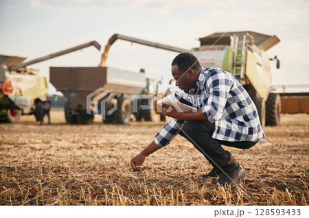 Opposite agricultural machinery. Beautiful African American man is in the agricultural field 128593433