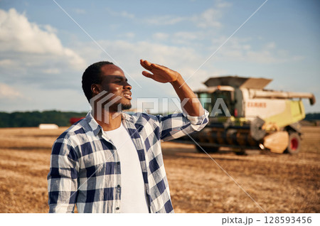 Machinery behind. Beautiful African American man is in the agricultural field Machinery behind. Beautiful African American man is in the agricultural field 128593456