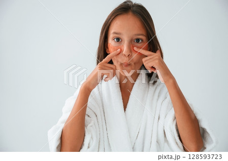 Orange colored eye patches on the face. Conception of beauty and self care. Young girl is in the studio Orange colored eye patches on the face. Conception of beauty and self care. Young girl is in the studio 128593723