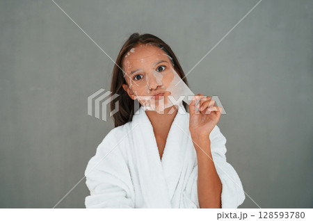 Funny facial expression. Playing with mask. Conception of beauty. Young girl is in the studio Funny facial expression. Playing with mask. Conception of beauty. Young girl is in the studio 128593780