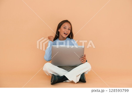 Sitting with laptop. Showing gesture. Cute young girl is in the studio against background Sitting with laptop. Showing gesture. Cute young girl is in the studio against background 128593799