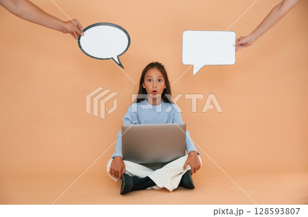 Thoughts stickers above. Sitting with laptop. Cute young girl is in the studio against background Thoughts stickers above. Sitting with laptop. Cute young girl is in the studio against background 128593807