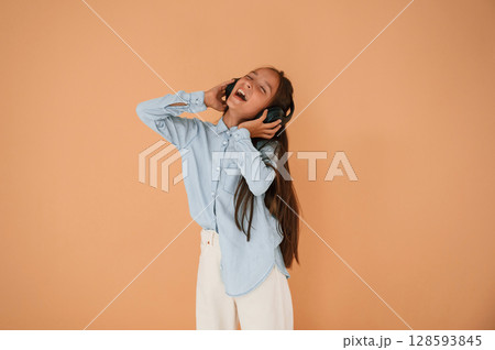 Enjoying the music, in headphones. Cute young girl is in the studio against background Enjoying the music, in headphones. Cute young girl is in the studio against background 128593845