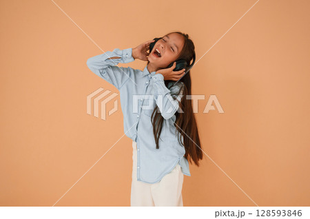 Enjoying the music, in headphones. Cute young girl is in the studio against background Enjoying the music, in headphones. Cute young girl is in the studio against background 128593846