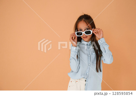 In stylish glasses. Cute young girl is in the studio against background In stylish glasses. Cute young girl is in the studio against background 128593854