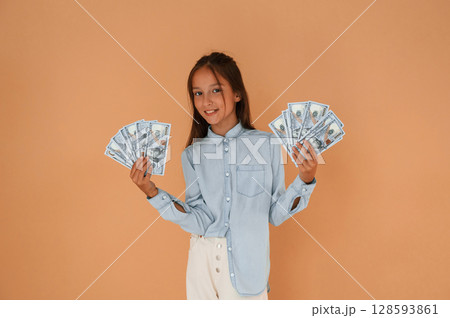 With bunch of currency, rich. Cute young girl is in the studio against background 128593861