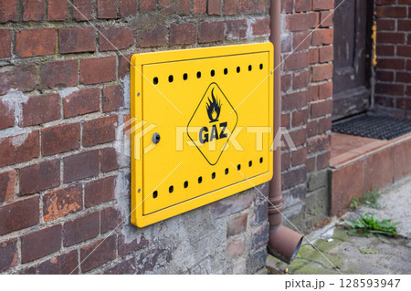 Bright yellow gas meter box displaying GAZ text and flame symbol mounted on an aged brick wall, symbolizing residential energy supply and essential utility infrastructure 128593947